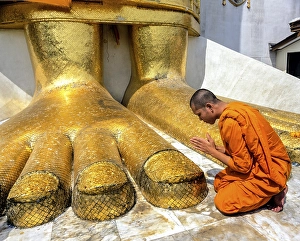 Monk praying at the feet of the golden Buddha statue of Wat Intharawihan