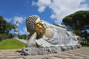 Monumental reclining Buddha statue in a green and peaceful park under a clear blue sky