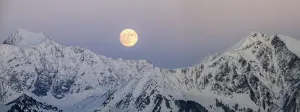 full moon rising into a blue sky in a winter mountain landscape in the Alps of Switzerland