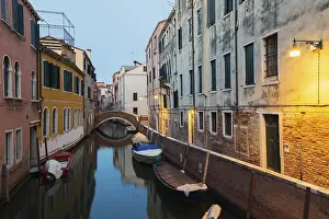 Moored boats and footbridge over Rio de la Toletta Canal with old architectural style residential buildings at dusk