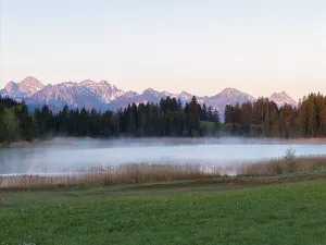 Morning fog hovers over a lake with mountain panorama in the background