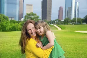 Mother and daughter happy hug laughing in park at city modern skyline background