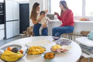Two mothers are chatting and drinking juice in a modern kitchen