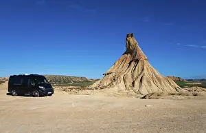 Motorhome in a barren desert landscape with striking rock formations and a clear blue sky