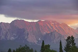 Mountain peak in bright red at sunset with dramatic clouds in the sky