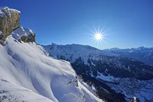 Mountain peak with snow-covered rocks under a clear blue sky with sun