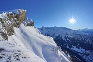 Mountain peak with snow-covered rocks under a clear blue sky with sun