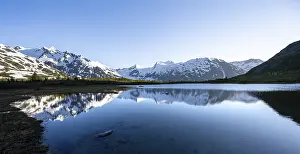 Mountain peaks with Portage Glacier glacier and snow reflected in Divide Lake mountain lake in evening light