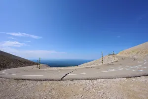 An empty mountain road with a hairpin bend under a clear blue sky and barren landscape