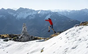 Mountaineer jumping, next to a cairn