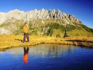 Mountaineer in front of mountain scenery reflected in a frozen mountain lake