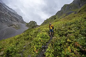 A mountaineer on a path surrounded by green vegetation and cloudy sky