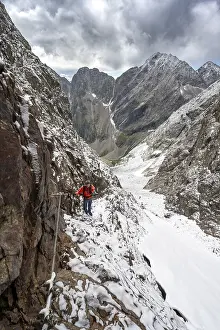 Mountaineer on a rope-secured path in a steep rocky mountain landscape with fresh snow in summer
