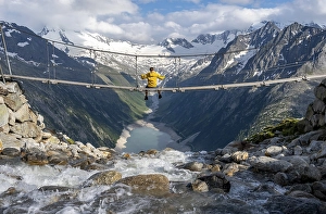 Mountaineer sitting on a suspension bridge over a mountain stream Alelebach