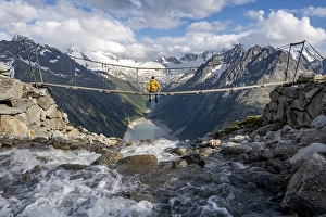 Mountaineer sitting on a suspension bridge over a mountain stream Alelebach