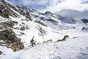 Mountaineer with skis climbing up a steep snow slope to the fork Porta d'Es-cha
