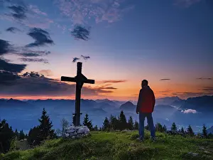Mountaineer standing next to the summit cross of the Ahornbuechsenkopf at dawn