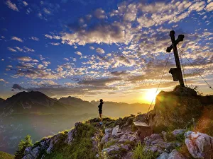 Mountaineer standing at sunset at the summit cross of the Brettgabel