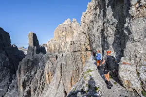 Three mountaineers on an exposed rock band in the secured Via Ferrata Bocciere Centrale via ferrata
