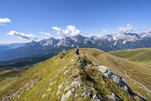 Mountaineers on a hiking trail between green mountain meadows on a mountain ridge