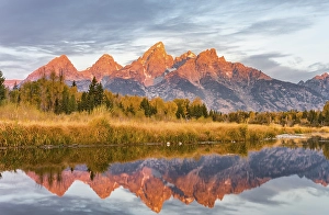 Mountains glow red at sunrise, Grand Teton Range mountain range reflected in the river