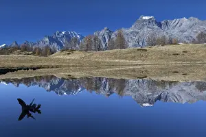 Mountains and a tree trunk are reflected in a calm lake under a clear blue sky