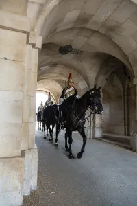 Mounted guards in black uniforms ride in formation beneath the stone arches during the daily Changing of the Guard