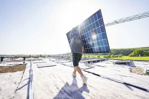 Moving worker with solar panel in front of a sunny landscape on a roof