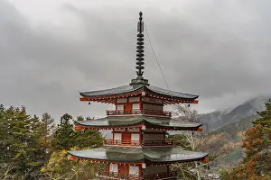 A multi-story Japanese pagoda rises against a cloudy sky surrounded by nature
