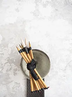 Multiple bamboo paint brushes tied with a black ribbon are resting on a ceramic bowl on a textured gray surface