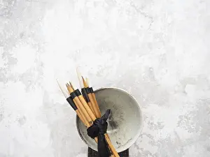 Multiple calligraphy brushes tied together with a black ribbon are resting on a ceramic bowl
