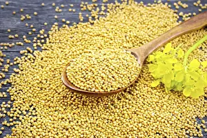 Mustard seeds in a spoon and on a table with a flower against a black wooden board