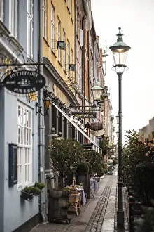 Narrow cobblestone street lined with cafes and colorful buildings under a vintage lamp post in Nyhavn