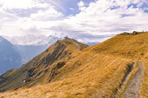 A narrow path leads over an autumnal mountain ridge under a cloudy sky