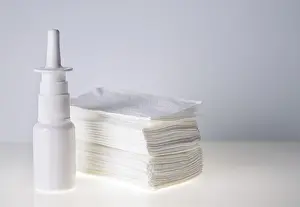 Nasal drops in a white bottle and a stack of handkerchiefs on a white background