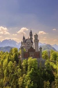 Neuschwanstein Castle amidst green trees in front of a clear sky and mountain scenery