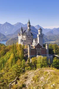 Neuschwanstein Castle surrounded by colourful autumn forests with a mountain panorama