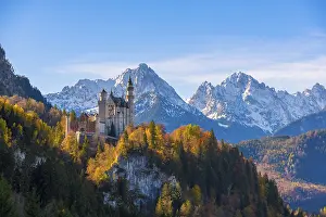 Neuschwanstein Castle towers over autumn trees against a backdrop of the Alps