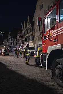 Night shot of a fire engine in front of half-timbered buildings with emergency services in the town