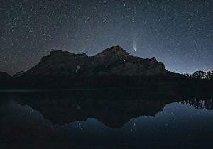 Night sky with stars over a mountain and its reflection in a calm lake