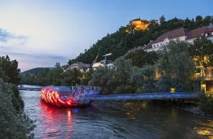 Night-time view of the Murinsel floating island on the river Mur with Schlossberg castle hill in the background