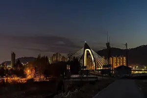 Night view of concrete bridge with triangular arch over a river with community buildings in background