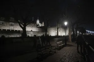 A nighttime view of a historic castle with a path lined by benches and lamps at The Tower of London