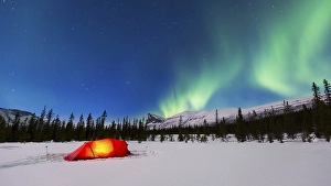 Northern Lights (Aurora borealis) above a red illuminated tent in winter