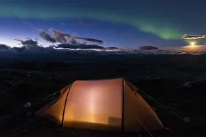 Northern lights and moonlight over an illuminated tent with a view of the Parma massif