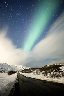 Northern lights over road with snow mountains
