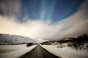 Northern lights over road with snow mountains