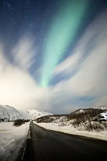 Northern lights over road with snow mountains