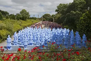 Numerous blue terracotta soldier statues stand on a path lined with flowers and trees