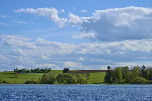 Ober- Moosersee surrounded by green fields and trees under a partly cloudy blue sky